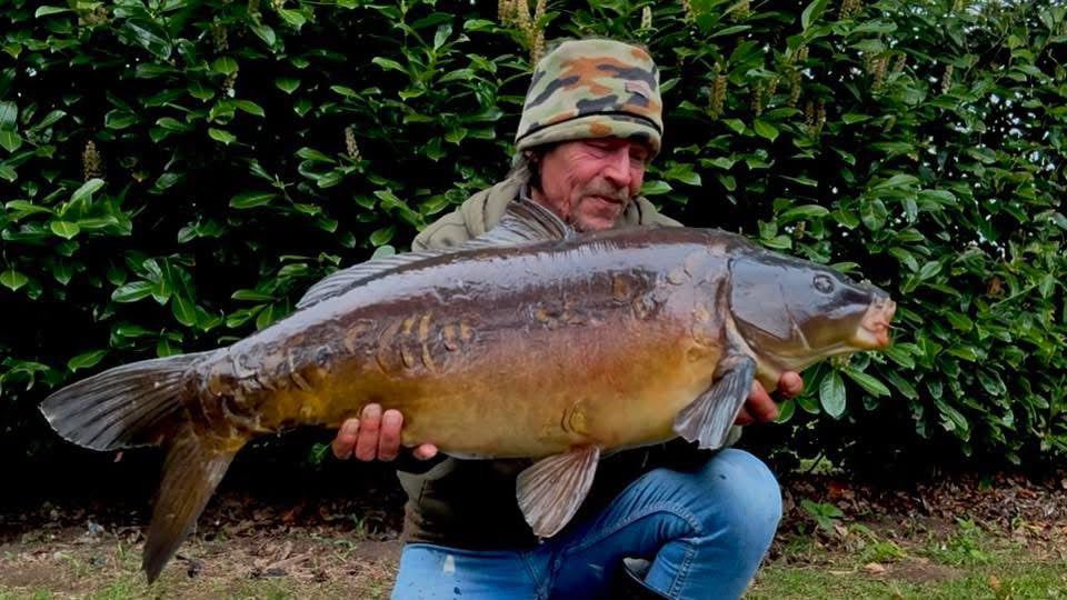 Man holding a large fish in front of a green hedge