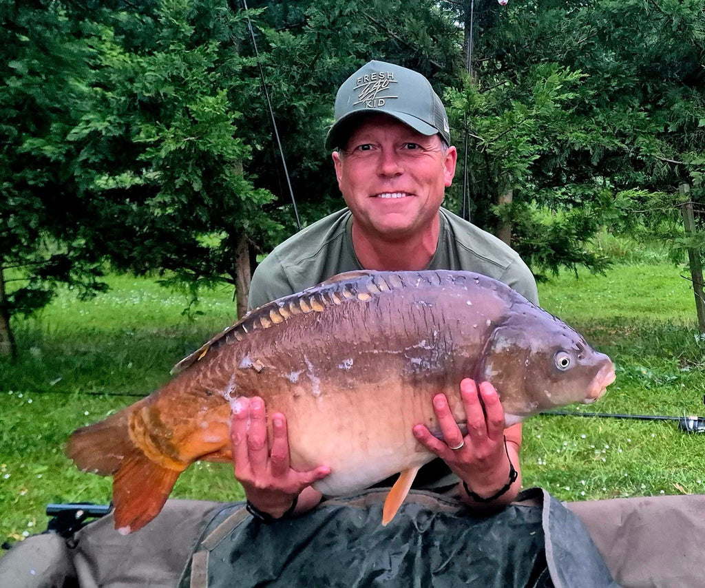 Man holding a large fish outdoors with greenery in the background
