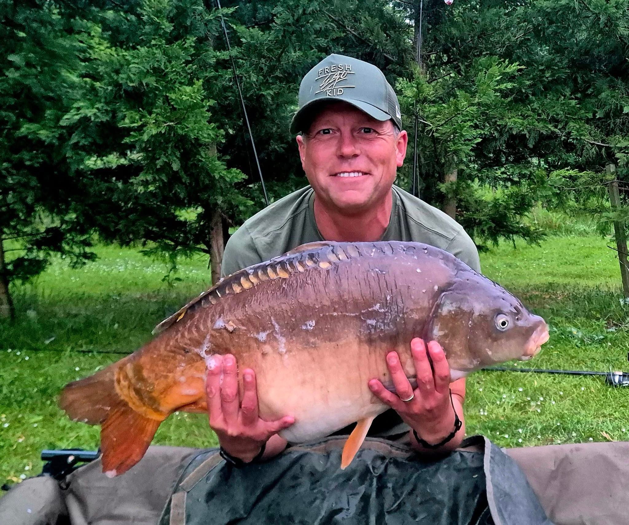 Man holding a large fish outdoors with greenery in the background