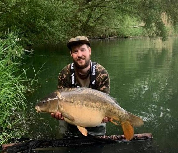 Man holding a large fish by a body of water with greenery