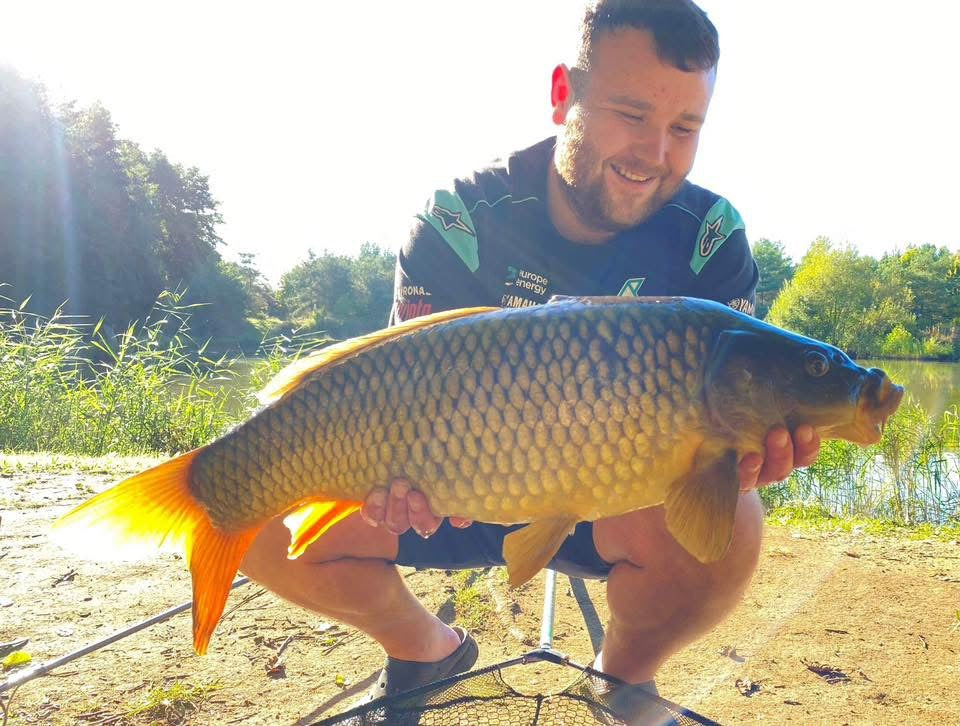 Man holding a large fish by a lake with trees in the background
