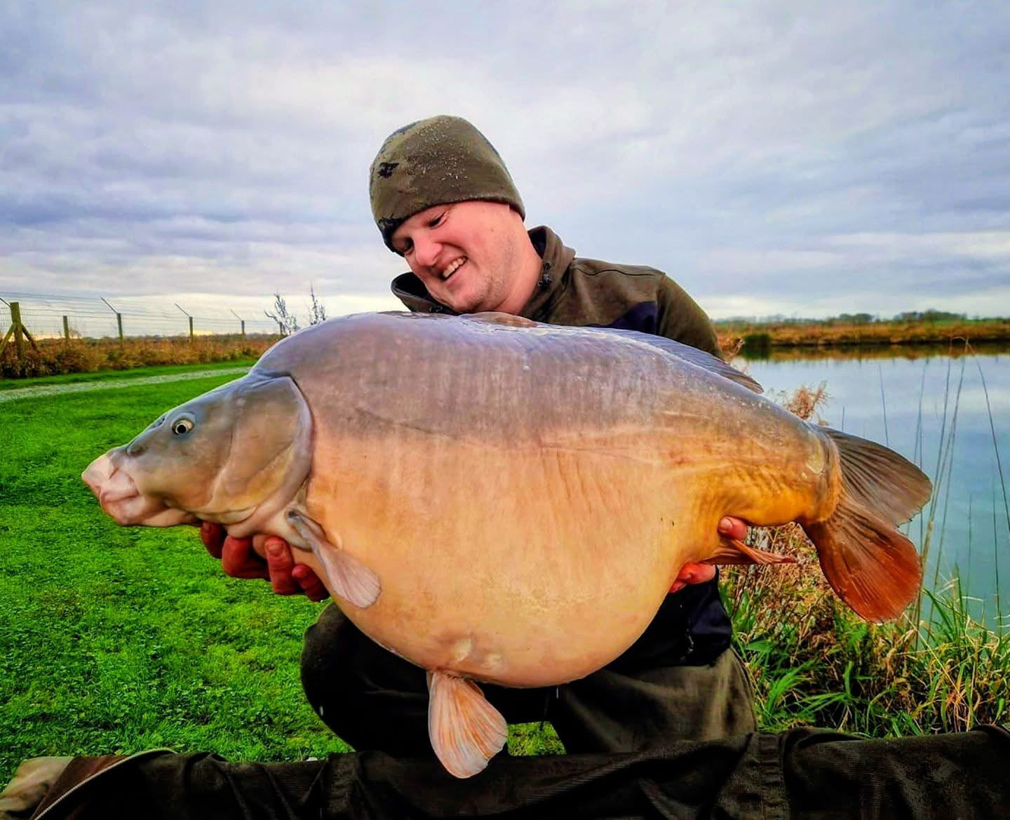 Man holding a large fish by a lake on a cloudy day