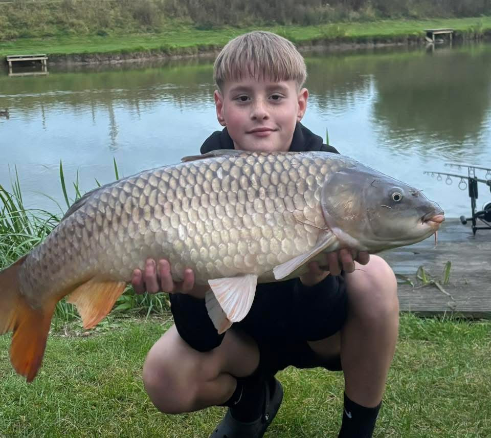 Young boy holding a large fish by a lake