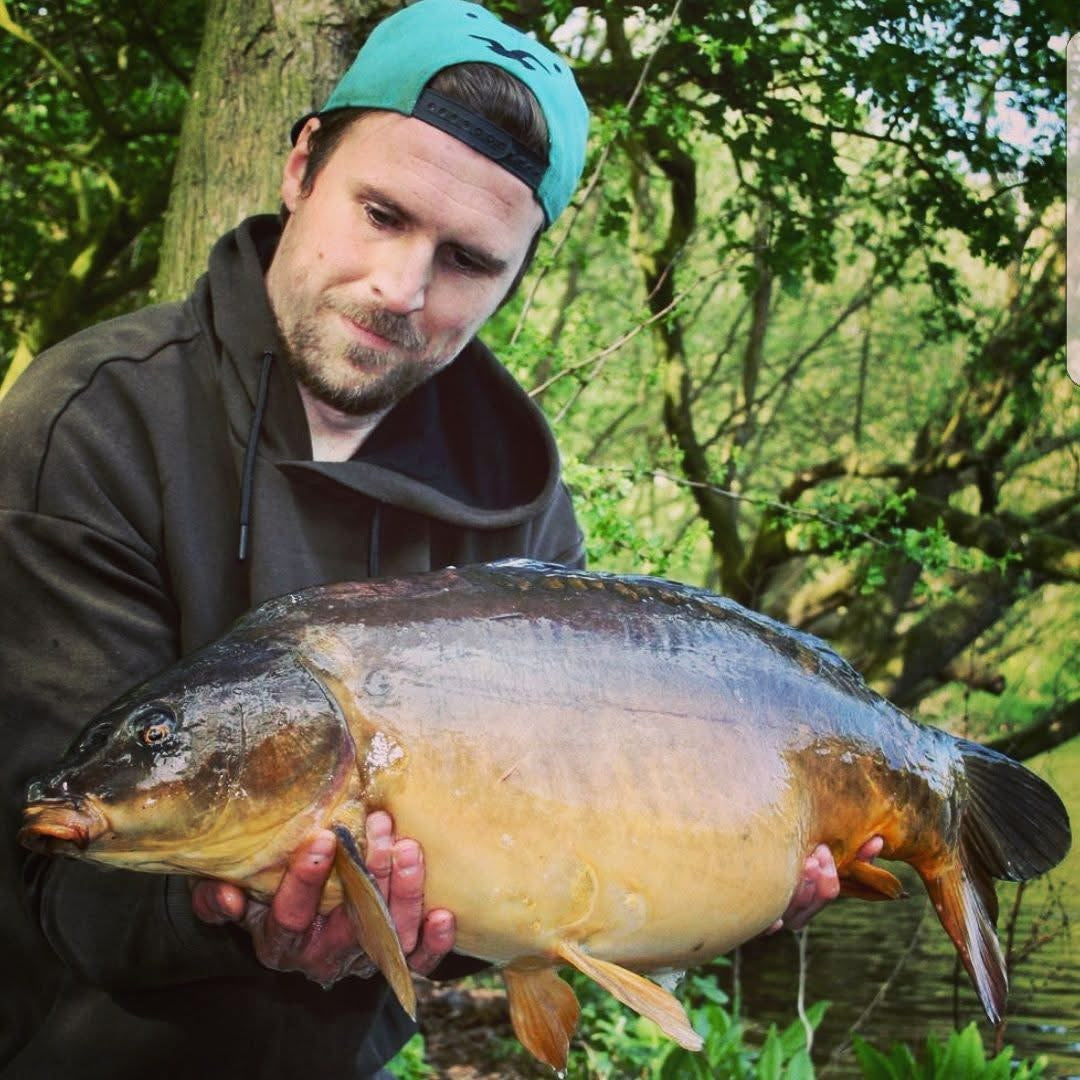 Man holding a large fish outdoors with trees in the background