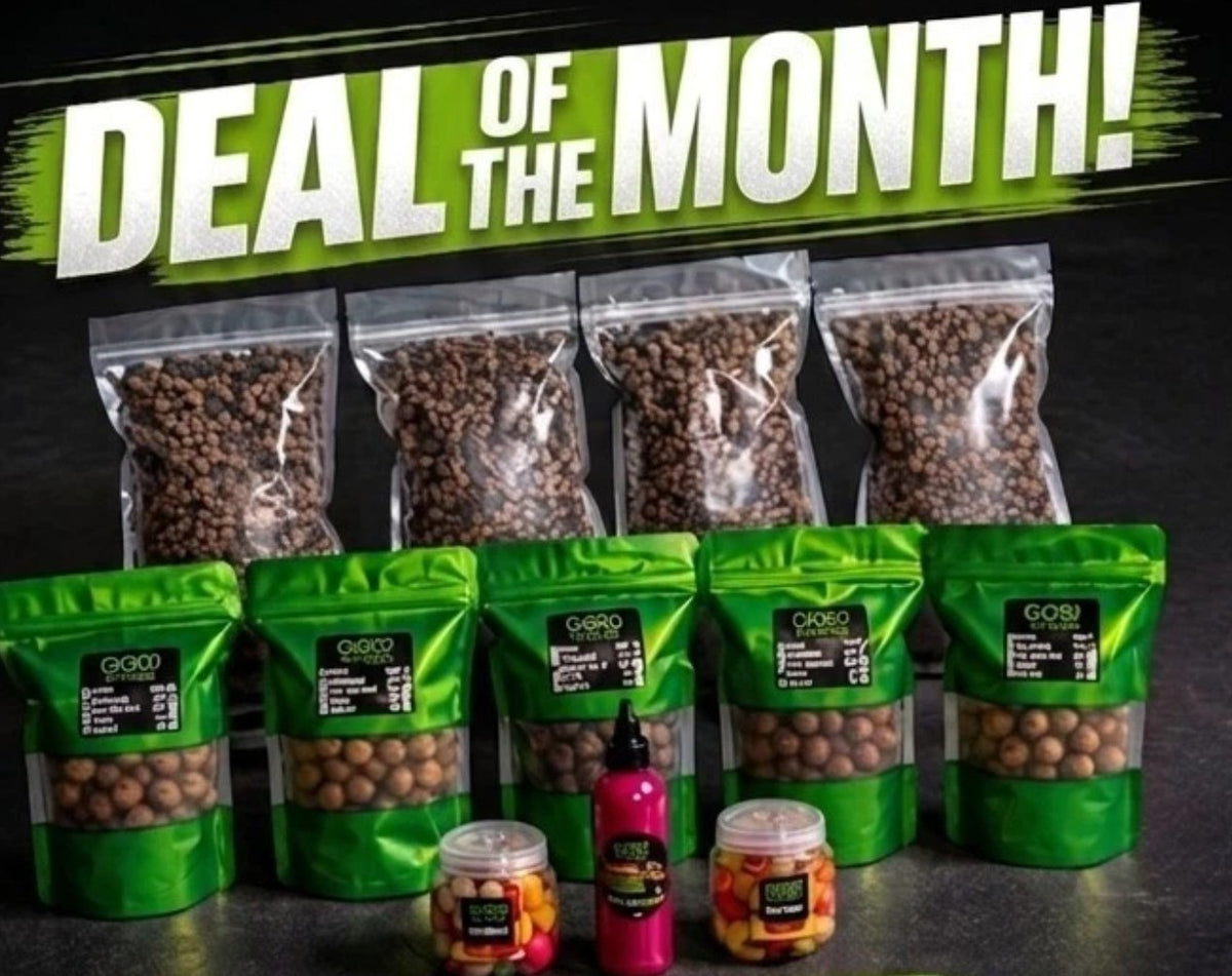 A promotional display of CCW baits, featuring multiple green resealable bags filled with boilies and pellets, two small jars of hookbaits, and a pink bottle of goo, all arranged on a dark surface beneath a large 'DEAL OF THE MONTH!' banner.