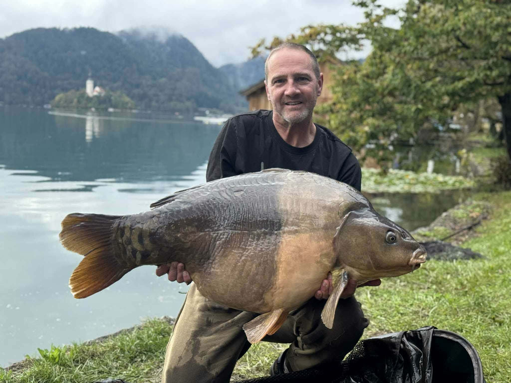 Man holding a large fish by a lake with mountains in the background